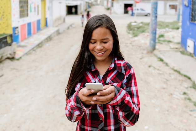 Portrait de jolie fille latino à l'aide du mobile dans un bidonville. Concept de l'enfance.