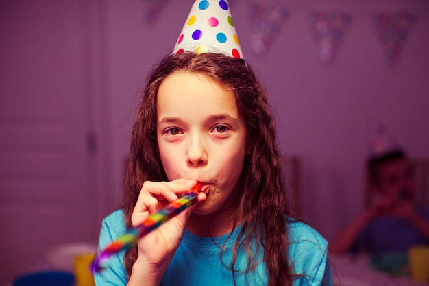 Portrait d'une jolie fille portant un chapeau de fête qui souffle dans une trompette