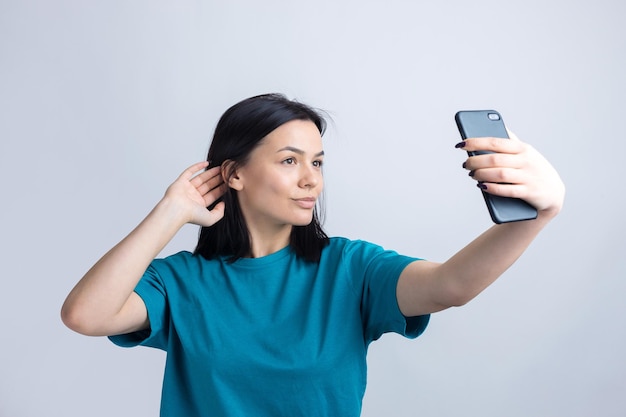 Portrait d'une jolie fille prenant un selfie isolé sur fond gris