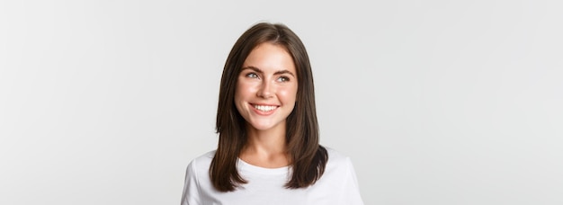 Portrait d'une jolie fille réfléchie souriante et regardant à gauche sur fond blanc