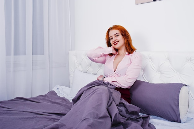 Portrait d'une jolie fille rousse allongée sur le lit et se couvrant d'une couverture violette
