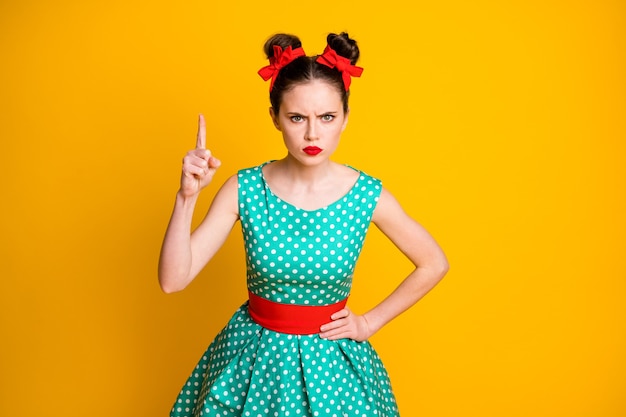 Photo portrait de jolie fille sérieuse stricte vêtue d'une robe bleu sarcelle pointillée menaçant l'index isolé sur fond de couleur jaune vif