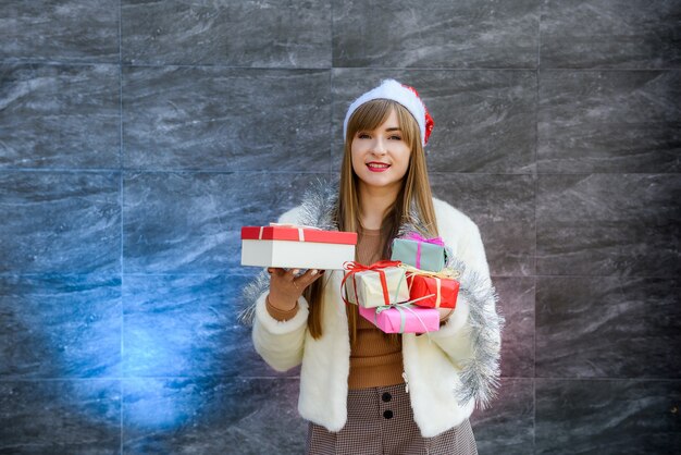 Portrait d'une jolie fille souriante tenant une pile de coffrets cadeaux sur fond gris