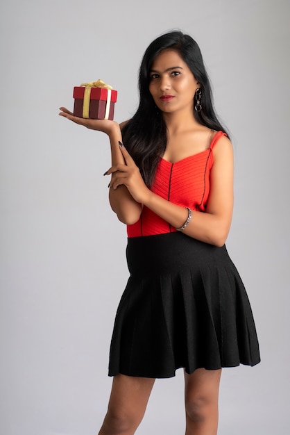 Portrait d'une jolie fille tenant et posant avec boîte-cadeau sur fond gris