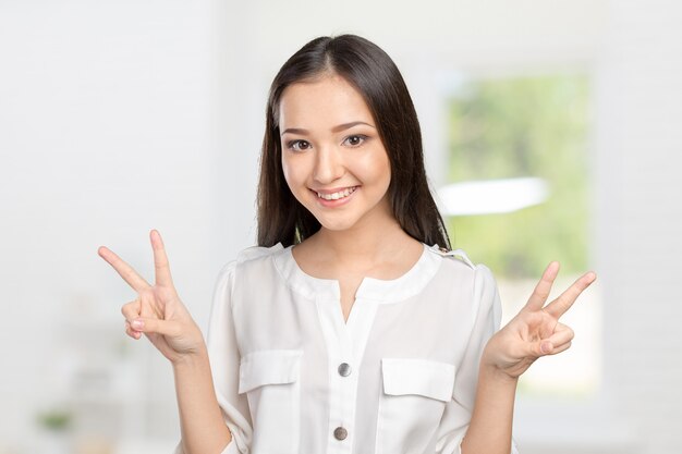 Portrait jolie jeune brune souriante montre le signe de la victoire