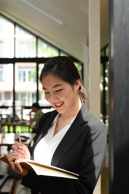 Portrait de jolie jeune femme d'affaires écrit sur un bloc-notes et standind dans la salle de réunion.