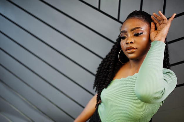 Portrait de jolie jeune femme afro-américaine portant un pull vert posant contre un mur gris