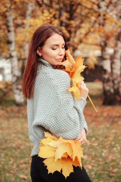 Portrait d'une jolie jeune femme d'apparence slave avec des feuilles en tenue décontractée en automne, debout sur fond d'un parc d'automne. Jolie femme marchant dans le parc en automne doré. Espace de copie