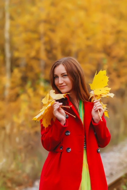 Portrait de jolie jeune femme d'apparence slave en robe jaune et manteau rouge en automne, promenade en forêt