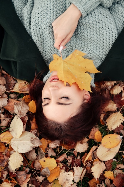 Portrait d'une jolie jeune femme d'apparence slave en tenue décontractée en automne, allongée sur des feuilles jaunes d'automne. Un modèle mignon se promène dans le parc en automne doré sur fond de nature. Espace de copie