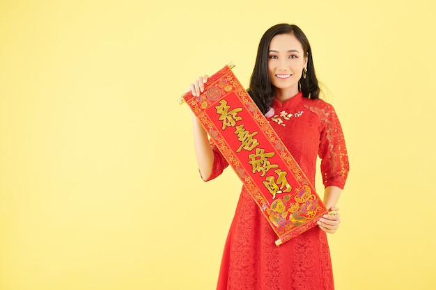 Portrait d'une jolie jeune femme asiatique tenant des couplets avec les meilleurs voeux comme décoration pour la célébration du Nouvel An chinois