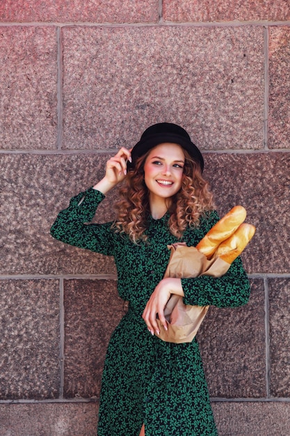 Portrait jolie jeune femme avec baguette dans les mains sur la texture de fond du mur. Une fille habillée à la française montre de l'émotion avec du pain. Femme dans des vêtements élégants tenant des baguettes fraîches. Espace de copie