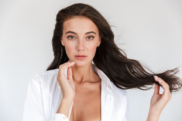 Portrait d'une jolie jeune femme brune souriante portant une chemise blanche isolée, posant