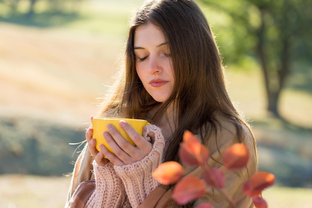 Portrait d'une jolie jeune femme en chandail tricoté élégant debout sur la forêt d'automne dorée aux beaux jours Il est temps de se détendre et de prendre un café