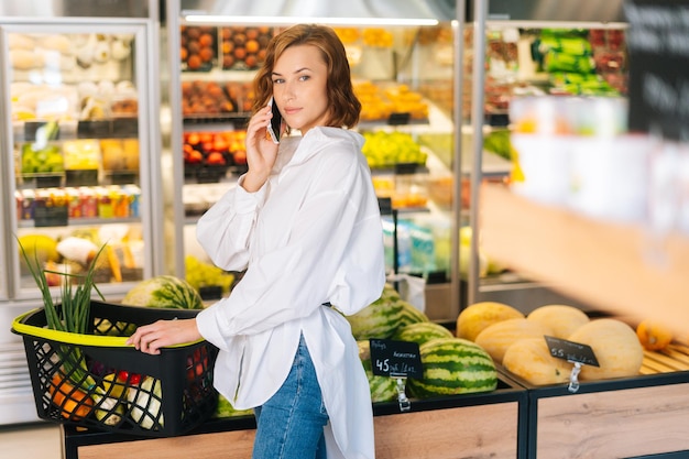 Portrait d'une jolie jeune femme cliente parlant sur un téléphone portable profitant de l'épicerie au supermarché Jolie femme heureuse choisissant des produits dans l'histoire de l'épicerie et parlant sur un smartphone