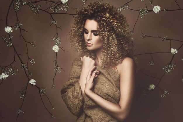 Portrait d'une jolie jeune femme avec une coiffure afro et un beau maquillage avec beaucoup de fleurs blanches sur fond