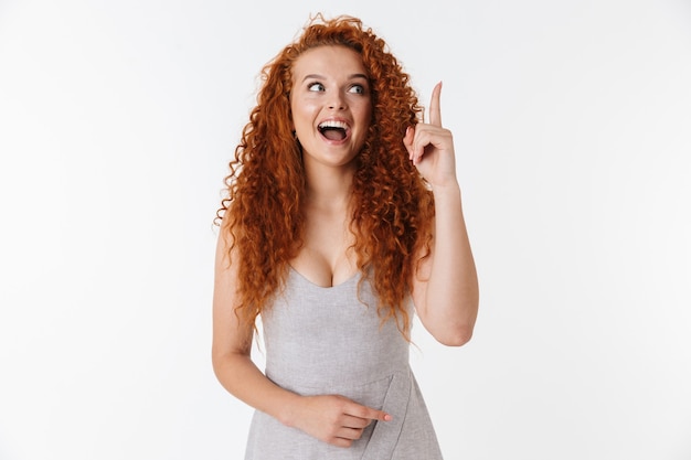 Portrait d'une jolie jeune femme excitée avec de longs cheveux roux bouclés isolés, présentant un espace de copie