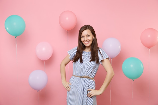 Portrait D'une Jolie Jeune Femme Heureuse Souriante Vêtue D'une Robe à Rayures Bleues, Debout Près De Ballons à Air Colorés Sur Fond Rose Tendance Brillant. Fête D'anniversaire, Concept D'émotion Sincère.