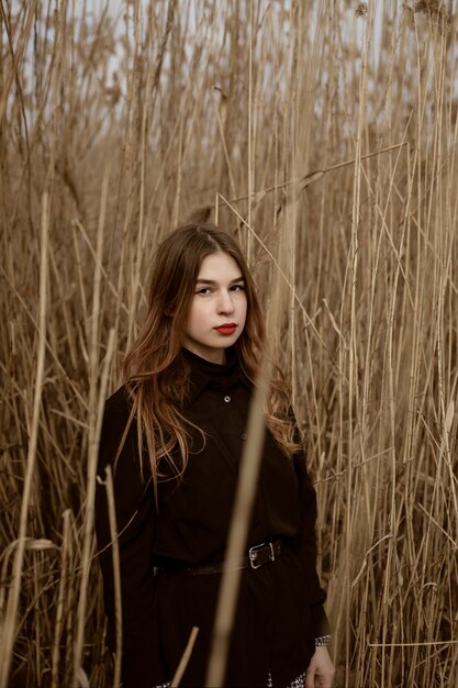 Portrait d'une jolie jeune femme marchant à l'extérieur près du lac, vêtue de vêtements noirs, champ élevé