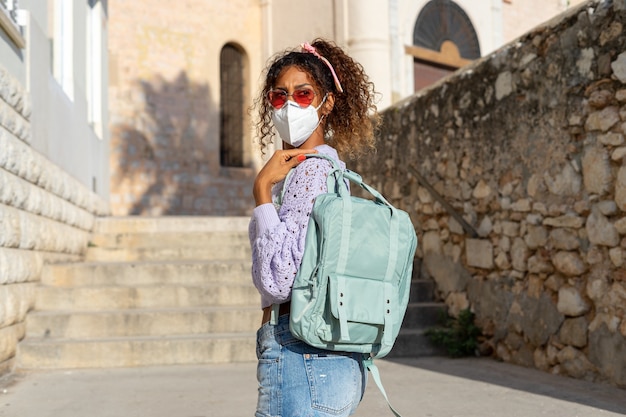 Photo portrait d'une jolie jeune femme noire marchant avec sac à dos et masque. tourisme