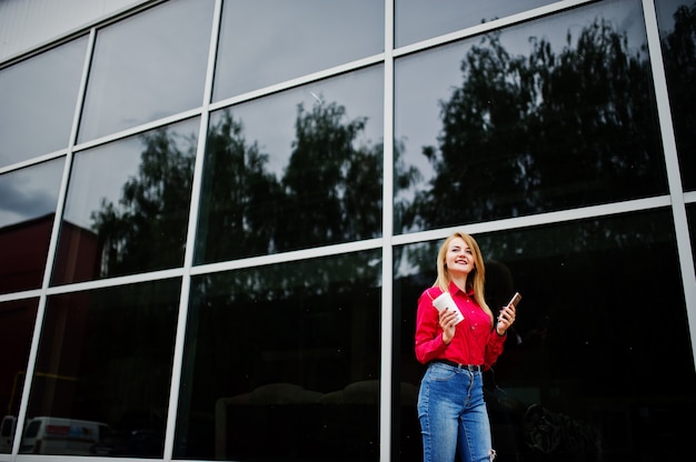 Portrait d'une jolie jeune femme posant avec café et smartphone en dehors du centre commercial.