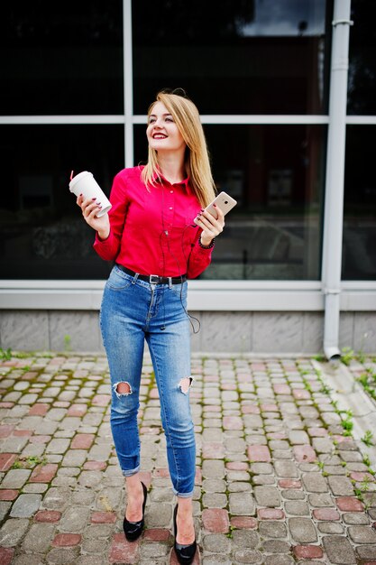 Portrait d'une jolie jeune femme posant avec café et smartphone en dehors du centre commercial.