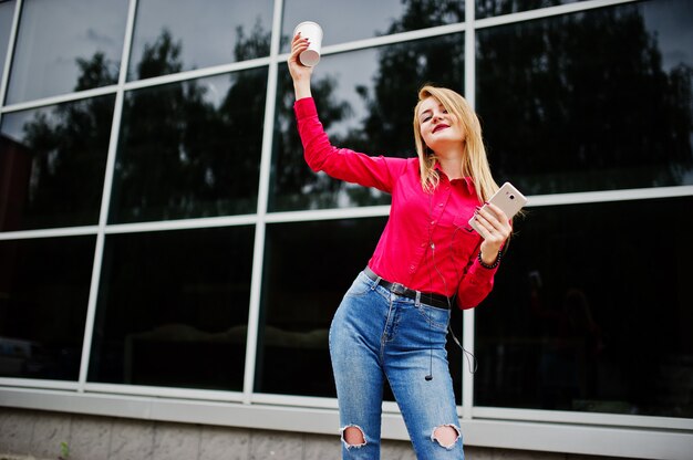 Portrait d'une jolie jeune femme posant avec café et smartphone en dehors du centre commercial.