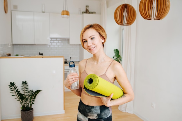 Portrait d'une jolie jeune femme posant avec un tapis de yoga et un verre d'eau