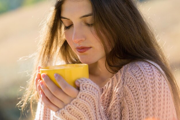 Portrait de jolie jeune femme en pull tricoté élégant debout avec une tasse jaune