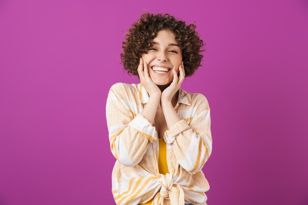 Portrait d'une jolie jeune femme souriante aux cheveux bouclés brune debout isolé sur un mur violet, riant