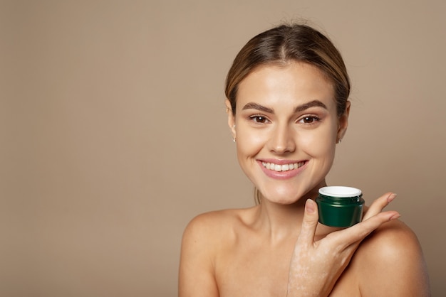 Portrait d'une jolie jeune femme souriante avec une peau fraîche et propre en studio sur fond beige.