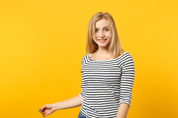 Portrait d'une jolie jeune femme souriante en vêtements rayés debout, regardant la caméra isolée sur fond de mur orange jaune en studio. Émotions sincères des gens, concept de style de vie. Maquette de l'espace de copie.