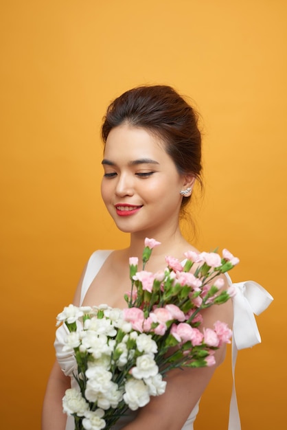 Portrait d'une jolie jeune femme tenant un bouquet d'oeillets isolé sur fond jaune