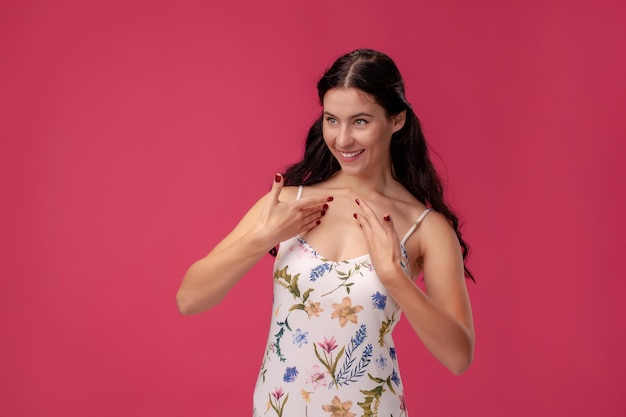 Portrait d'une jolie jeune femme vêtue d'une robe légère debout sur fond rose en studio. Les gens émotions sincères.