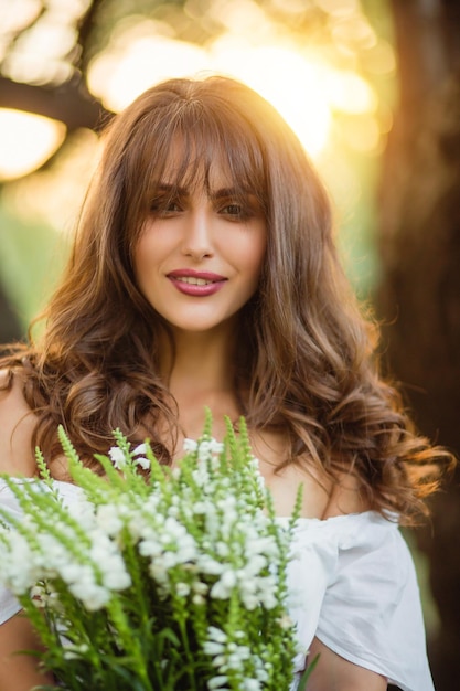 Portrait d'une jolie jeune fille avec un bouquet de fleurs au coucher du soleil