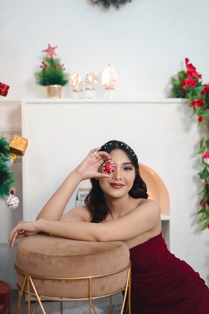 Portrait de jolie jeune fille confortable s'asseoir sur le sol en souriant porter une robe rouge dans le salon de Noël décoré à l'intérieur