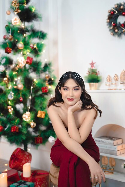 Portrait de jolie jeune fille confortable s'asseoir souriant porter une robe rouge dans le salon de Noël décoré à l'intérieur