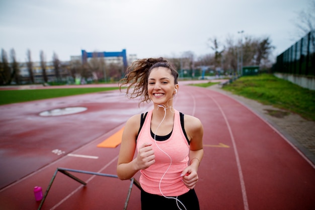 Portrait de jolie jeune fille fitness heureux jogging tout en écoutant de la musique à l'extérieur sur la piste de course.