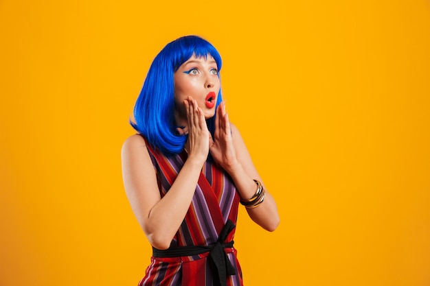 Portrait d'une jolie jeune fille funky aux cheveux bleus portant une tenue décontractée, isolée sur un mur jaune, en détournant les yeux