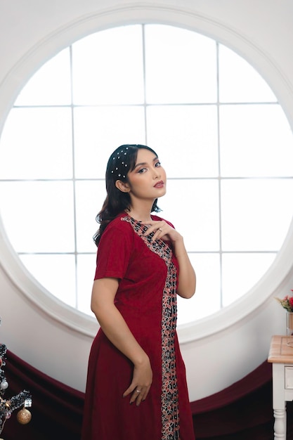 Portrait d'une jolie jeune fille portant une robe rouge souriant à la caméra debout dans le salon de Noël décoré à l'intérieur