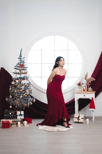 Portrait d'une jolie jeune fille portant une robe rouge souriant à la caméra debout dans le salon de Noël décoré à l'intérieur