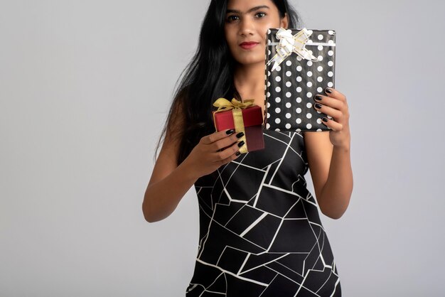 Portrait d'une jolie jeune fille posant avec boîte-cadeau sur fond gris.