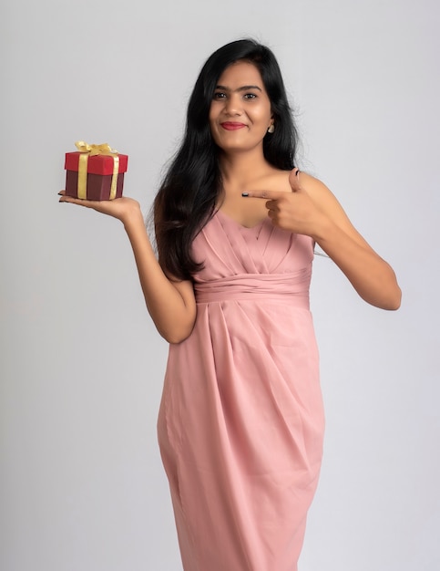 Portrait d'une jolie jeune fille posant avec boîte-cadeau sur fond gris.