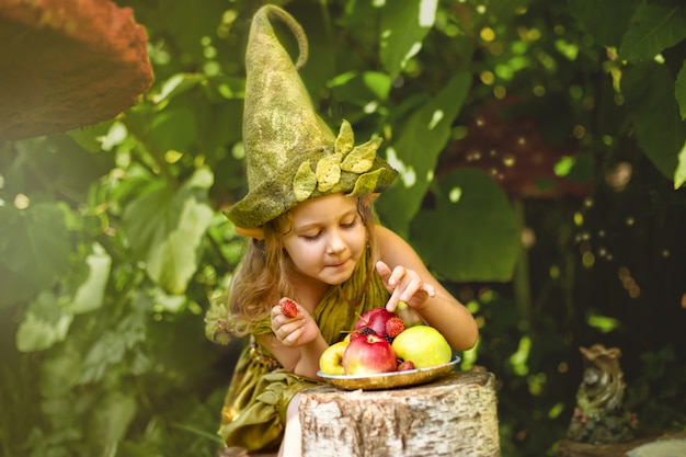 Portrait d'une jolie jolie fille dans un gnome mange des baies et des pommes sur une plaque.
