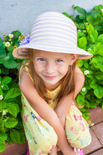 Portrait de jolie petite fille au chapeau assise au jardin