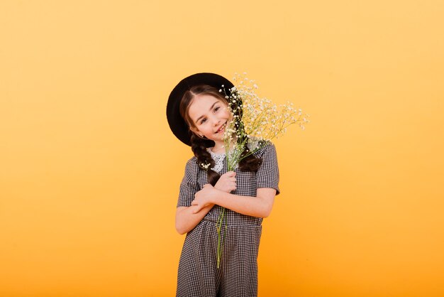 Portrait de jolie petite fille avec bouquet de fleurs en studio sur fond jaune. Félicitation, printemps ou concept de joyeuses fêtes. Copier l'espace pour le texte