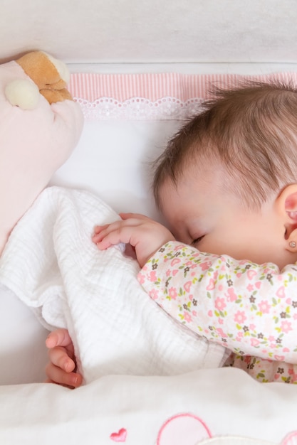 Portrait d'une jolie petite fille dormant dans un lit bébé avec tétine et peluche