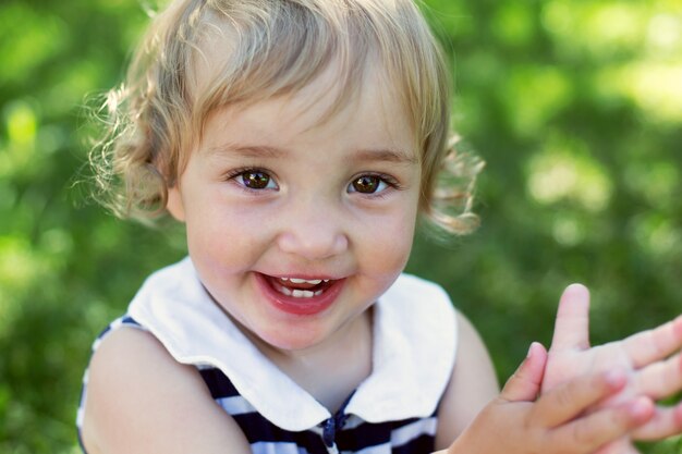 Portrait d'une jolie petite fille heureuse et bouclée en journée d'été ensoleillée contre l'herbe verte