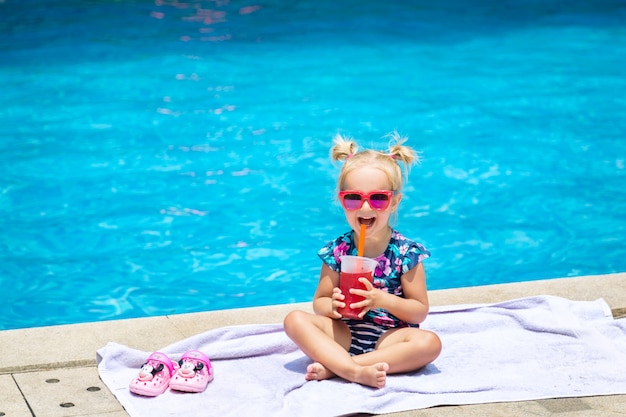 Portrait de jolie petite fille heureuse s&#39;amuser dans la piscine et boire du jus de melon d&#39;eau