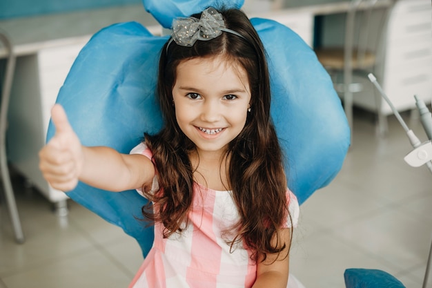 Portrait d'une jolie petite fille montrant le pouce après la chirurgie des dents. Happy kid après examen des dents dans une stomatologie pédiatrique.